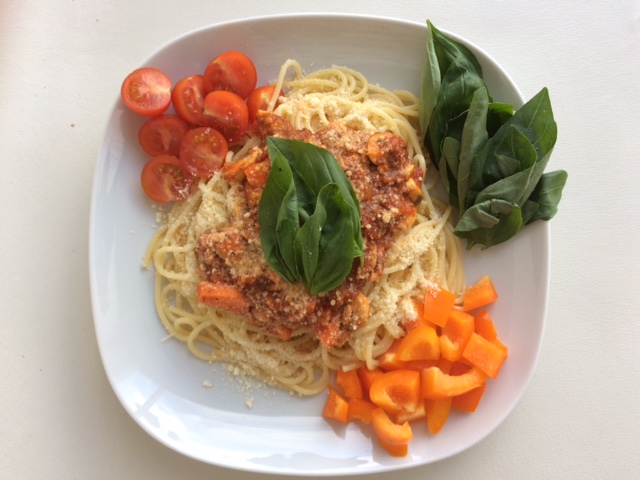 Spaghetti saus tomat wortel dan jamur disajikan dengan taburan keju, paprika, daun basil, dan tomat.